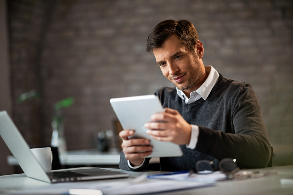 Happy businessman working on touchpad while being in the office. happy entrepreneur using digital tablet reading something while working office
